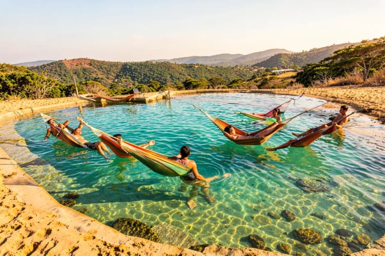 Pessoas relaxando em redes dentro de piscinas naturais em Jericoacoara com águas claras e calmas