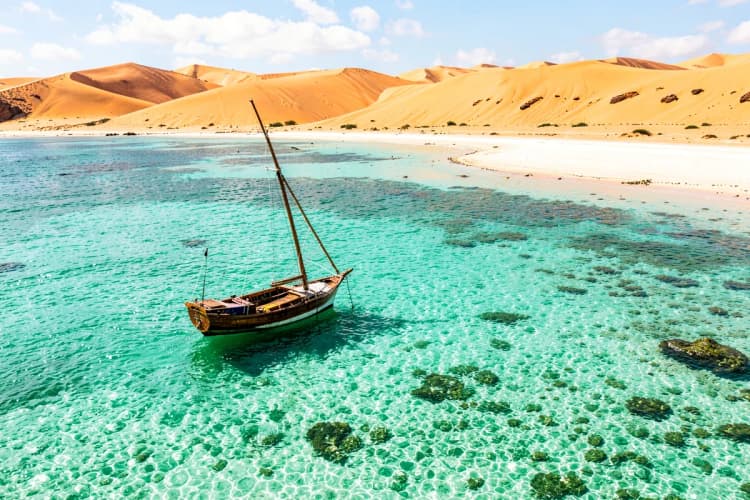 Vista aérea de barco navegando em águas cristalinas de Jericoacoara com dunas ao fundo