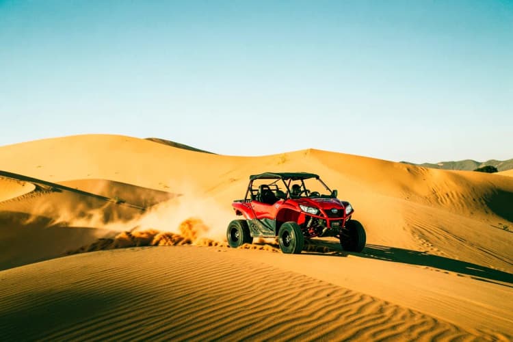 Buggy em alta velocidade pelas dunas douradas de Jericoacoara sob um céu azul.