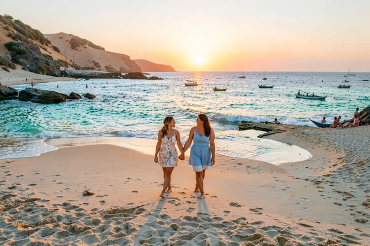 Casal caminhando de mãos dadas em uma praia de areia clara em Jericoacoara ao pôr do sol.