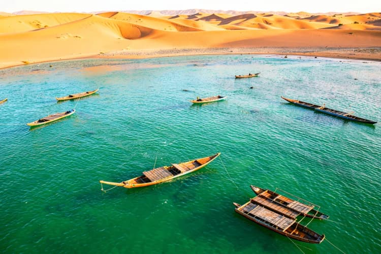 Vista aérea de jangadas coloridas navegando em águas cristalinas perto de dunas de areia em Jericoacoara.